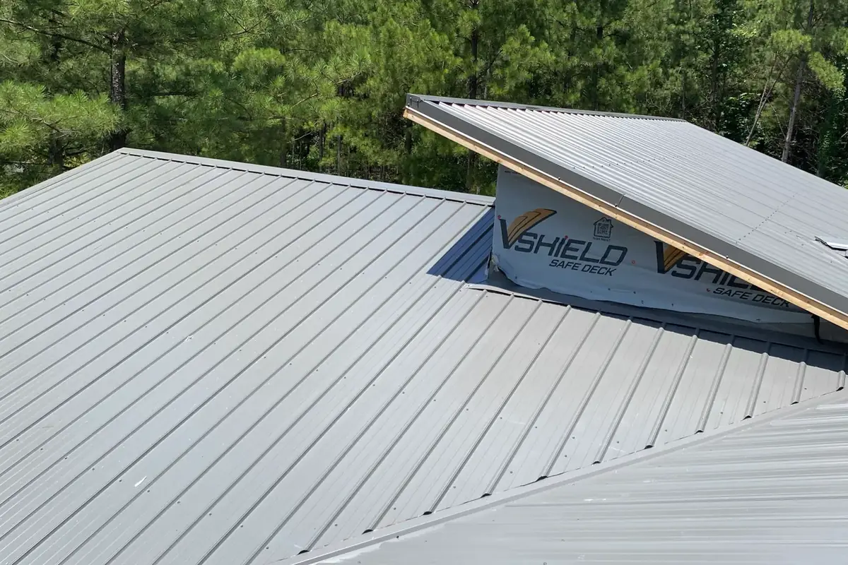 Gray ribbed metal roof where two roof levels meet, with wrap still showing on the wall between them