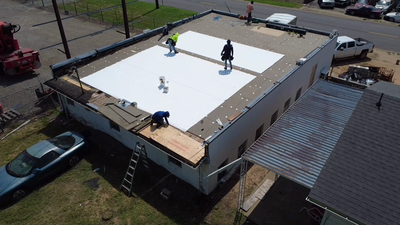 Crew rolling out white TPO membrane across a commercial flat roof