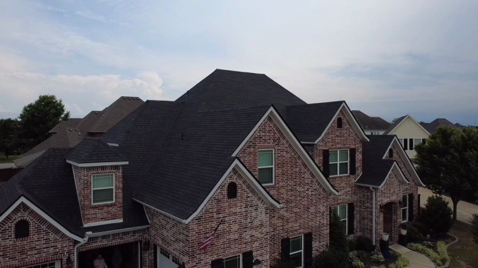 Aerial view of a finished dark shingle roof on a large brick home